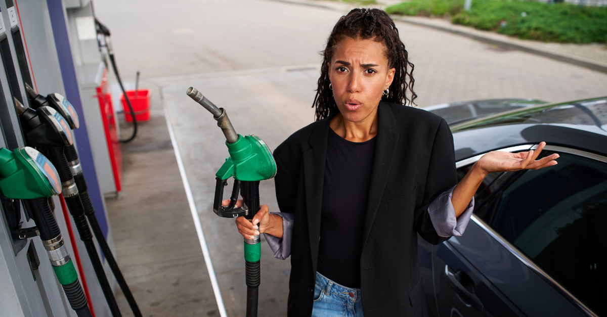 Frustrated driver reacting to expensive fuel bills while holding a dispenser handle at a petrol station