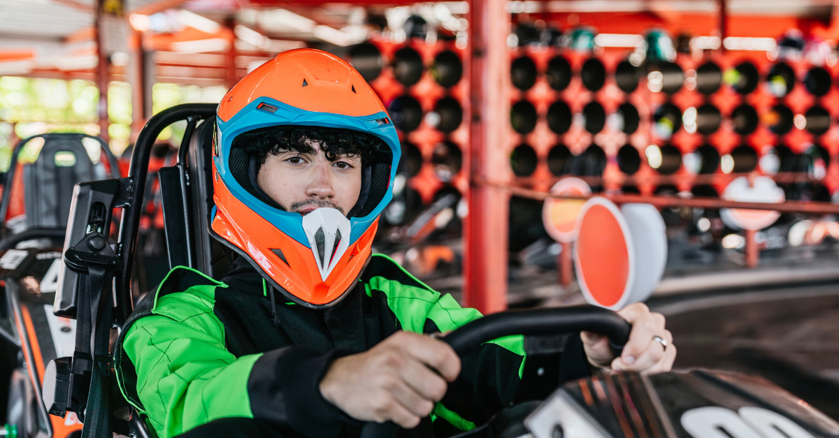 Young man wearing a safety helmet and racing suit, sitting in a go kart, preparing to race on a karting track