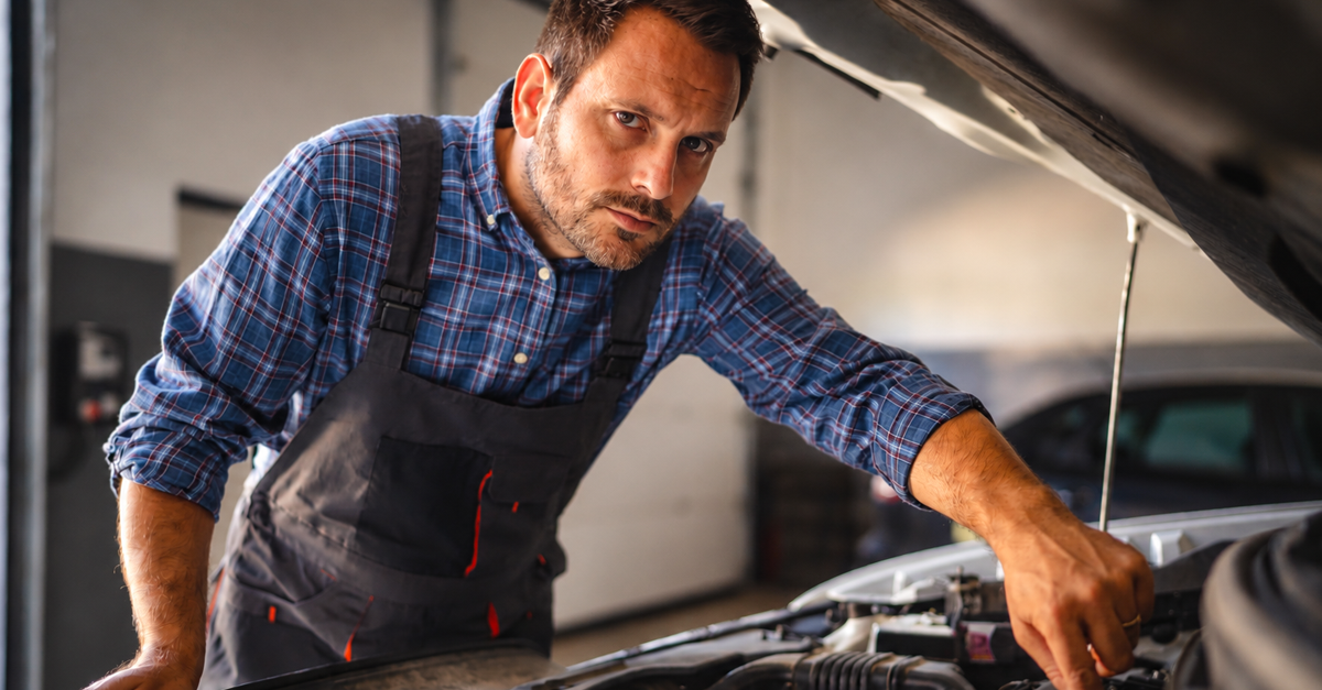 Adult man car mechanic work in a garage, use tools to repair a vehicle while the car hood is open