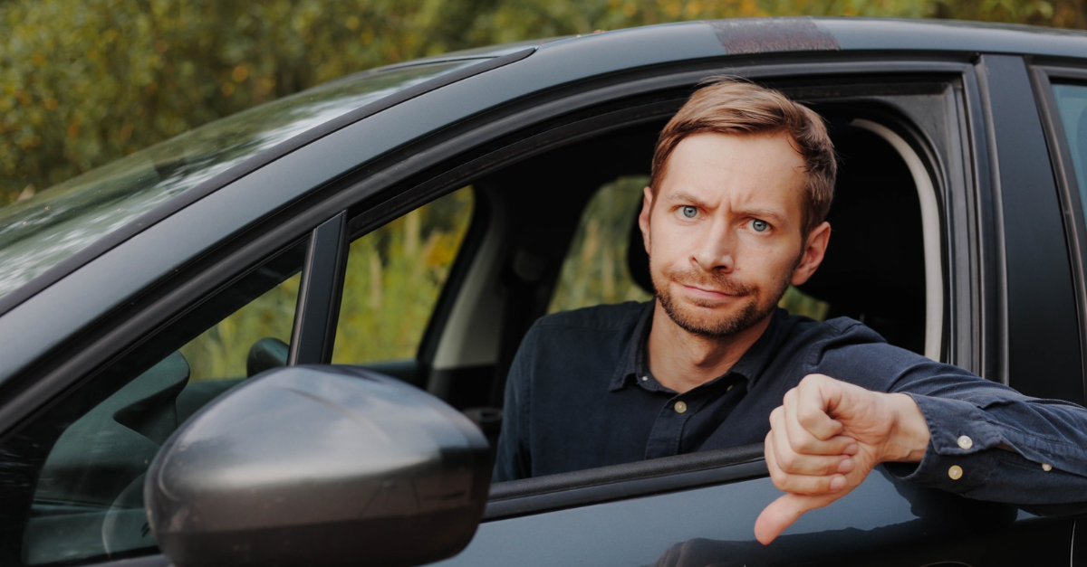 Unhappy driver showing thumbs down in car.
