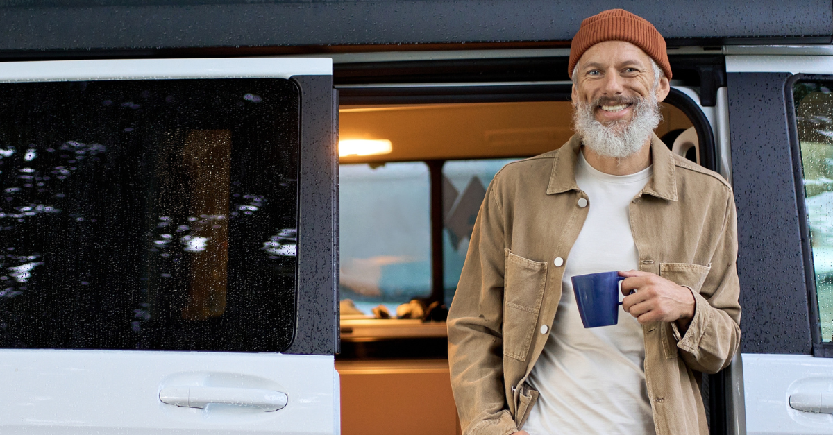 Happy older senior hipster man standing near rv camper van on vacation