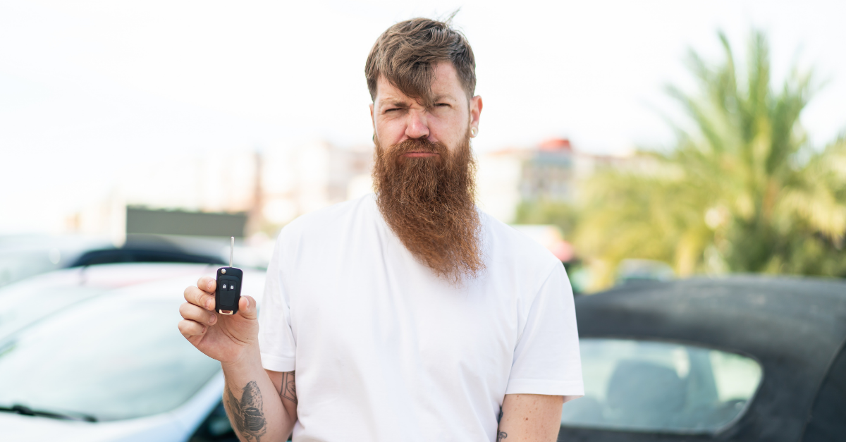 man with beard holding car keys at outdoors with sad expression