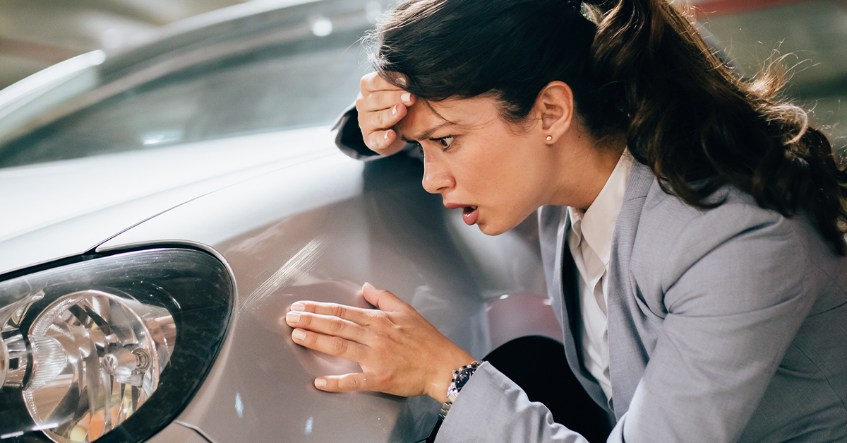 Woman looking at a scratch on her car.