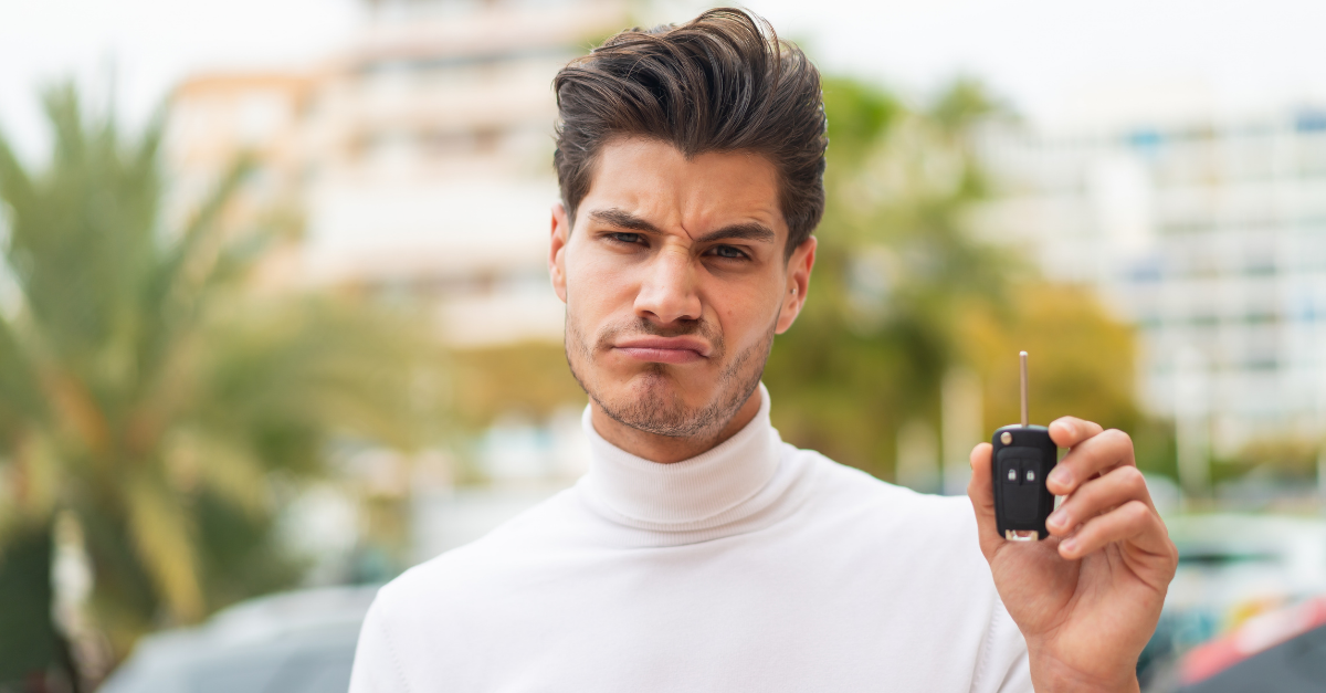 Young caucasian man holding car keys at outdoors with sad expression