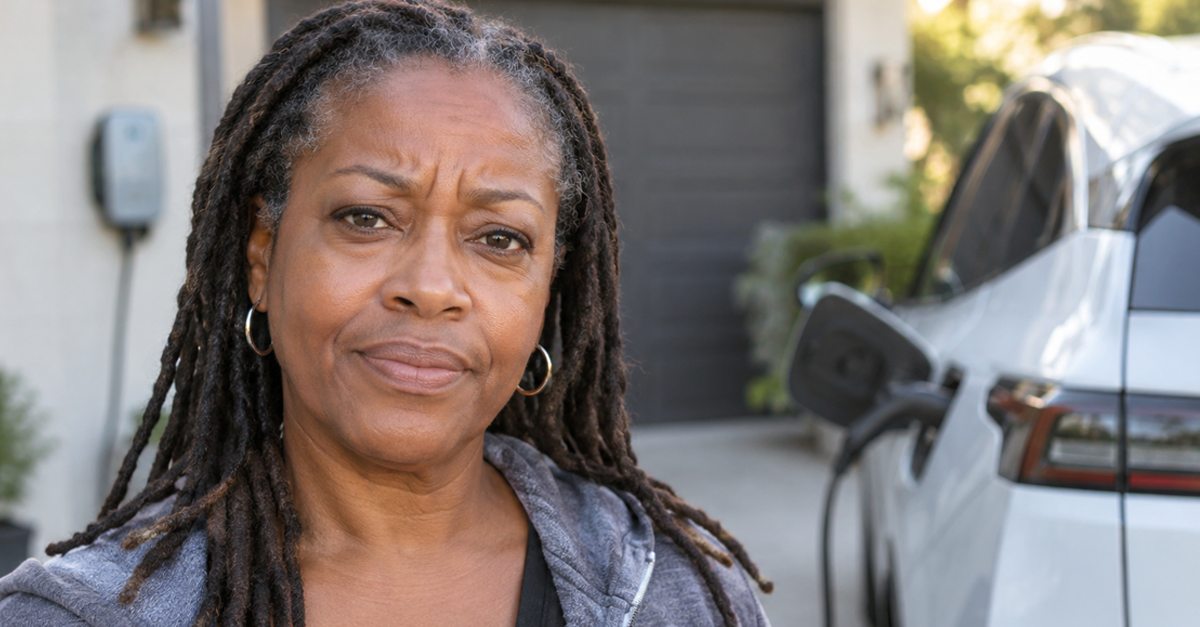 Frustrated woman on her driveway with an EV charging behind her